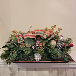 Pine trees and pine cones covered in snow along with a multi colored bow on a red tray.