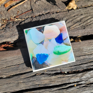 A 4x4 coaster with a picture of clear, blue, and green sea glass.
