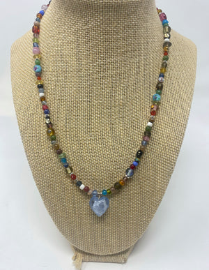 A necklace with a blue heart in the center. It is surrounded by multi color and size beads.