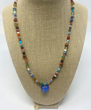 A necklace with a dark blue heart in the center. It is surrounded by multi color and size beads.