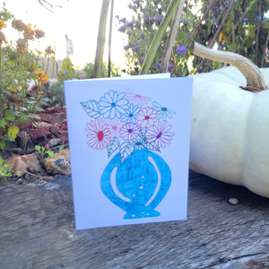 A white card with multicolored flowers in a blue round vase.