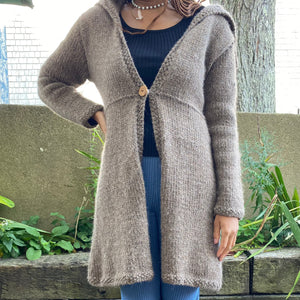 This a long light brown handknitted sweater that connects with a magnetic button.