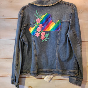 A denim jacket with a rainbow island and a pink flower vine across