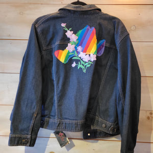 A denim jacket with a rainbow island and a pink vine flower.