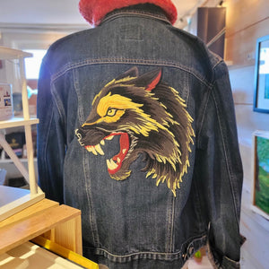 A denim jacket with a yellow and black wolf on the back