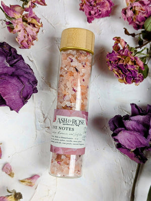 A vial filled with sea salt surrounded by dried rose and rose petals