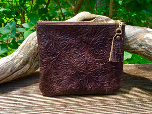 Brown coin purse leaning against driftwood in front of bushes.