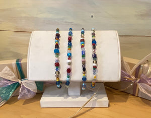 Four multicolor bead bracelets on a stand in front of a neutral background.