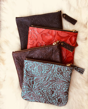 Four leather pouches in black, red,brown, and turquoise lying on a sheepskin background. 