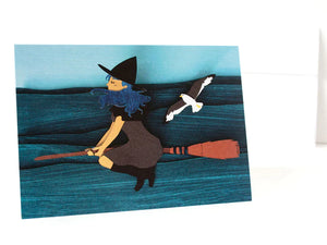 Paper cut depiction of  a witch flying on a broom above the sea