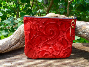 Red leather coin purse leaning against driftwood with bushes in the background.