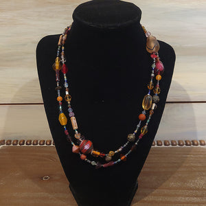 A long necklace with orange, red and brown chunky beads that vary in size.