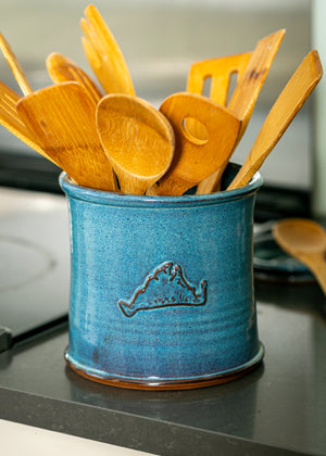 Blue hand thrown pottery utensil bucket with Martha's Vineyard shape on the side filled with wooden spoons sitting on a kitchen counter.