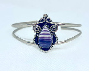 A silver cuff bracelet with a tear drop shaped purple quahog.