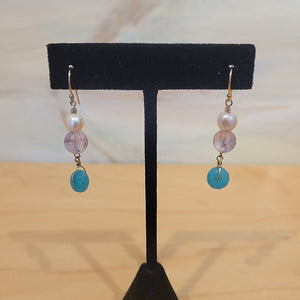 Gold earrings that have a pearl, a clear purple and a blue bead.